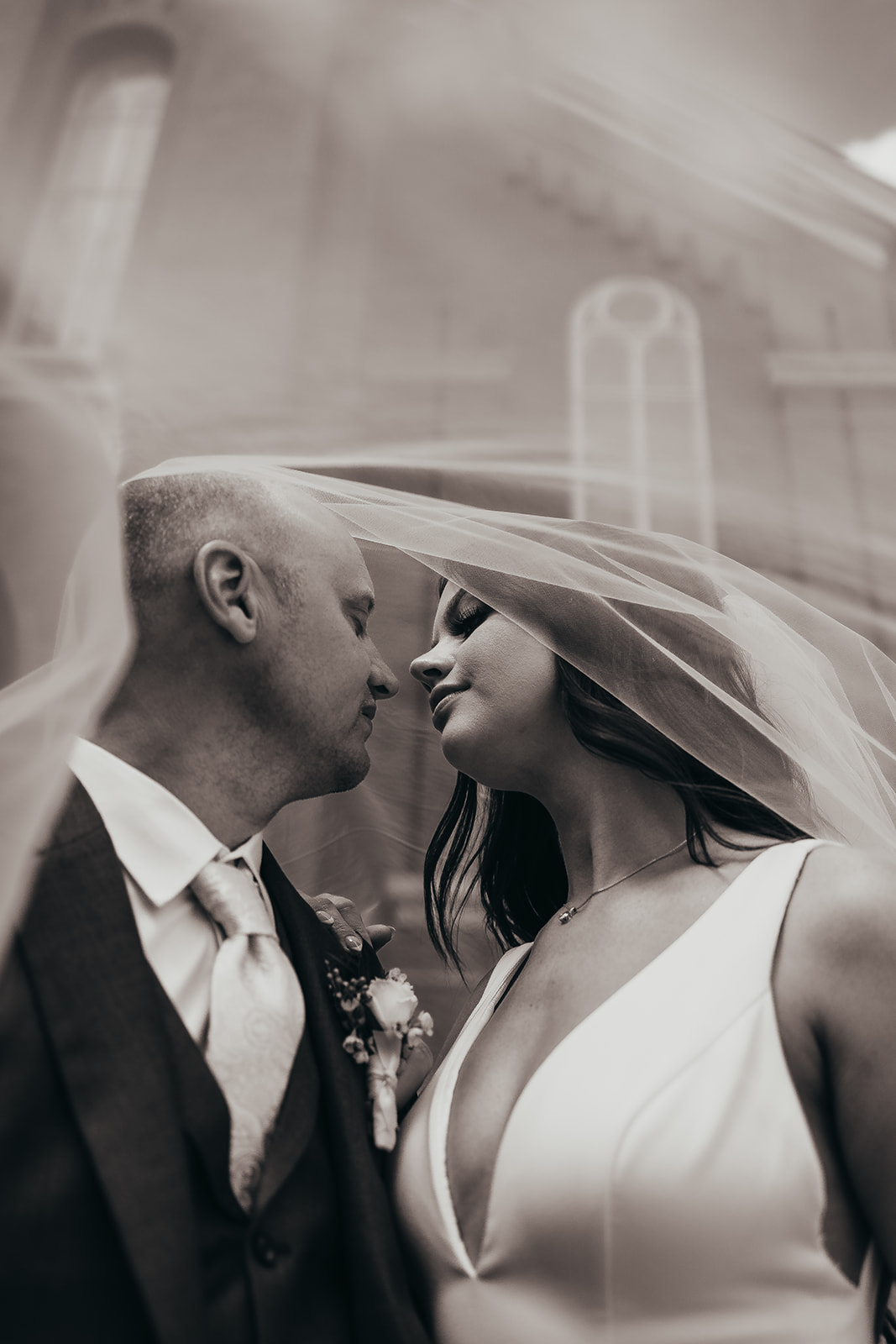 Allye and Andy forehead to forehead underneath her veil, photographed in black and white
